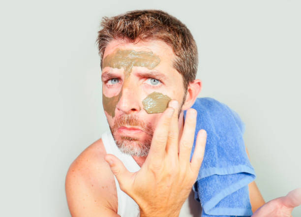 estilo de vida aislado retrato de joven atractiva y alegre con la toalla de baño con crema verde en el rostro aplicar mascarilla facial de belleza cuidado de la piel y uso de los cosméticos masculinos concepto - male towel men human face fotografías e imágenes de stock