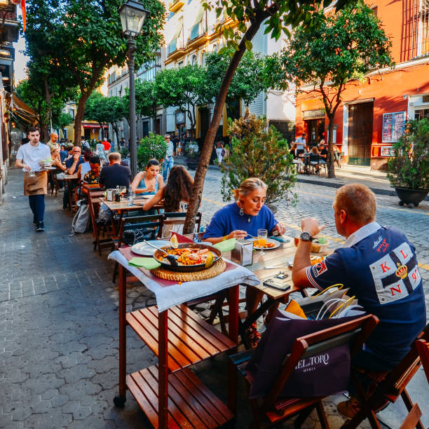 touristen genießen sie im restaurant terrasse typisch spanische küche, meeresfrüchte-paella mit muscheln, tintenfische, muscheln und garnelen auf einem bett eine aromatisierte safranreis - beer food paella clam stock-fotos und bilder