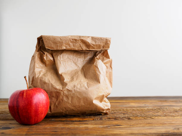 Paper bag with break bread and a red apple Food, fruit, school, table, white background, apple packed lunch photos stock pictures, royalty-free photos & images