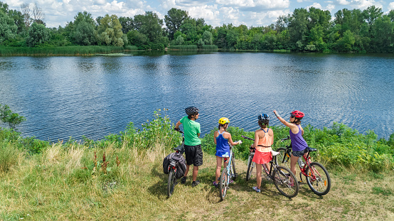 Family on bikes cycling outdoors, active parents and kids on bicycles, aerial view of happy family with children relaxing near beautiful river from above, sport and fitness concept