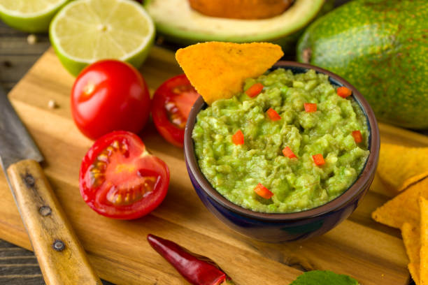 istock Guacamole in blue bowl on natural rustic desk with ingredient: lemon, tomatoes, peppers around. 1000952982