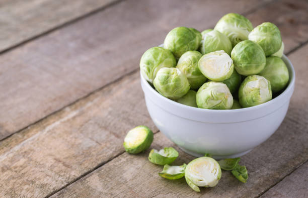 raw brussels sprouts in white bowl on wooden rustic desk. - head cabbage imagens e fotografias de stock