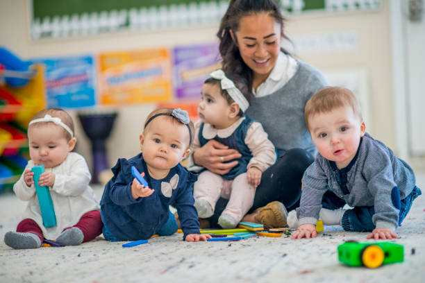 Toddlers with their caretaker A group of babies are indoors in a day care centre. They are sitting on the carpet and playing with toys. nursery school child stock pictures, royalty-free photos & images