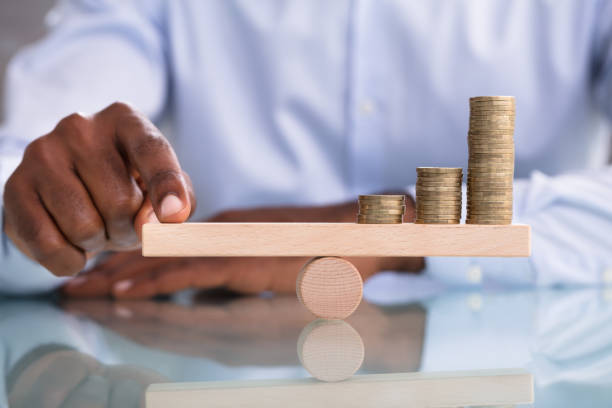 Businessman Balancing The Coin Stack On Wooden Seesaw