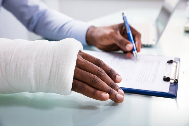 Injured Man Filling Insurance Claim Form Overhead View Of Injured Man With Bandage Hand Filling Insurance Claim Form On Clipboard claim form stock pictures, royalty-free photos & images