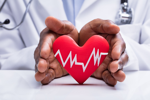 Close-up Of Doctor Protecting Heart With White Heartbeat Pulse Icon On White Desk