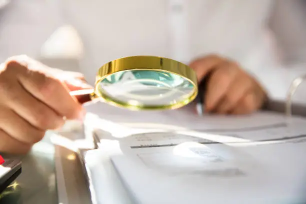 Businessman examining bill through magnifying glass in office