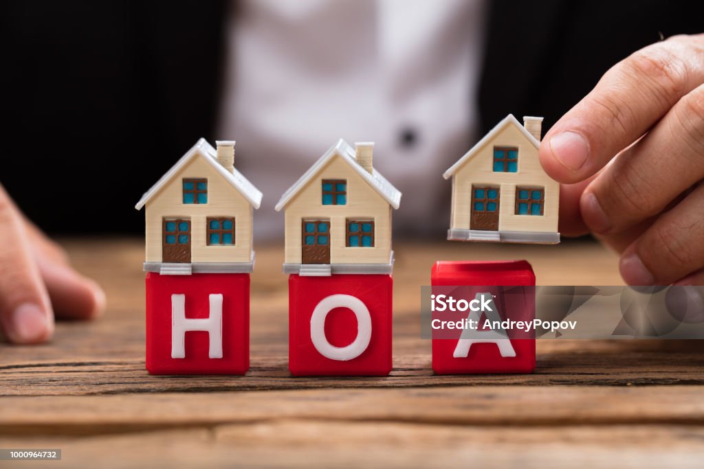 Businessperson placing house model over HOA blocks Businessperson's hand placing house model over red HOA blocks on wooden desk Home Ownership Stock Photo