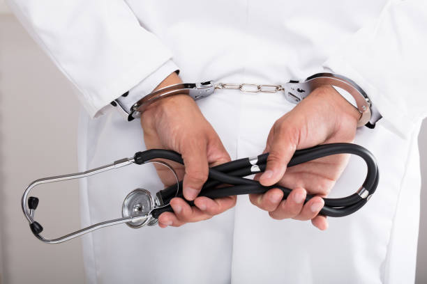 Doctor's hand with handcuff Doctor's hand with handcuff holding stethoscope behind white collar crime handcuffs stock pictures, royalty-free photos & images