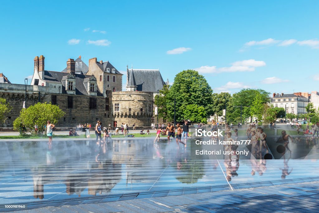 Children play in the fountain in front of the fortress in Nantes, France. The photo was taken on July 14, 2017 on the Day of the Bastille in Nantes, France. This fountain is located in front of the Breton Fortress in the city center. Nantes Stock Photo
