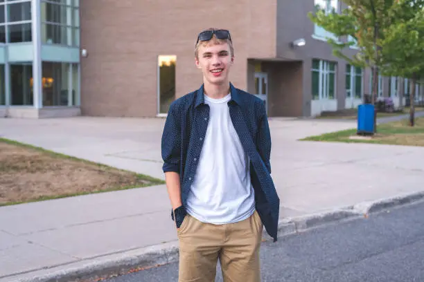 Photo of Happy teenager standing outside of a school in a parking lot.