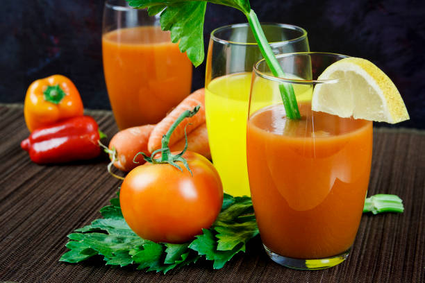 Orange juice and tomato juice in a dark background and pepper, carrots, tomatoes and celery leaf.