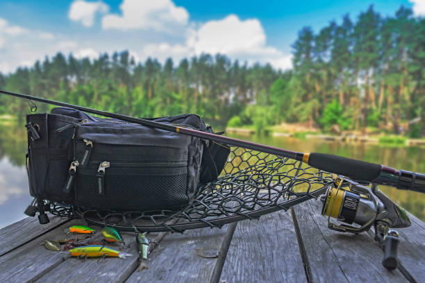 Fishing tackle set. Spinning rod with reel and lures on wooden platform on forest lake background Fishing tackle set. Spinning rod with reel and lures on wooden platform on forest lake background fishing gear stock pictures, royalty-free photos & images