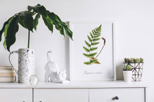 istock Creative cupboard with mock up poster frame, cat figure, tropical leaf and plant. White wall background. Modern scandinavian interior. 1001156654