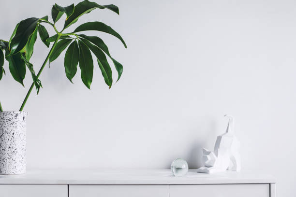 istock Minimalistic concept of white home interior whit copy space, tropical leaf and cat figures. Scandinavian white cupboard concept. 1001156658
