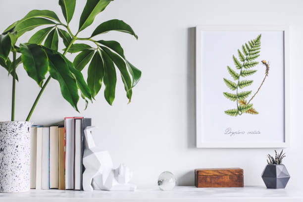 istock Creative cupboard with mock up poster frame, cat figures, tropical leaf and books. Modern and minimalistic concept of space. 1001156672
