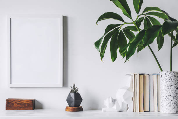 istock Scandinavian interior with white cupboard, mock up poster frame, cat figures, tropical leaf and books. Modern and minimalistic concept of space. 1001156682