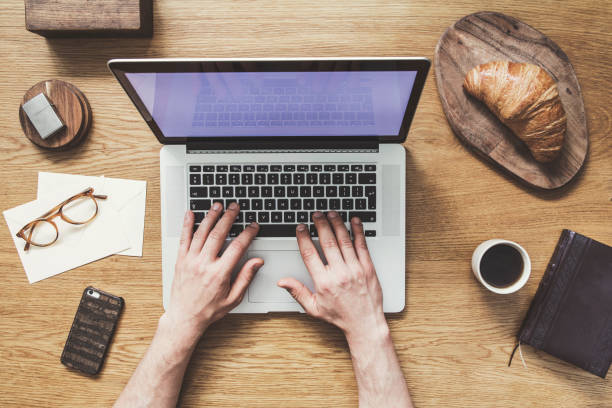 Modern and stylish composition of flat lay on wooden desk with laptop, croissant, cup of coffee, phone, notebook, glasses and office accessories. Hands writing on laptop keyborad. Creative desk . Concept of stylish flat lay desk. keyborad stock pictures, royalty-free photos & images