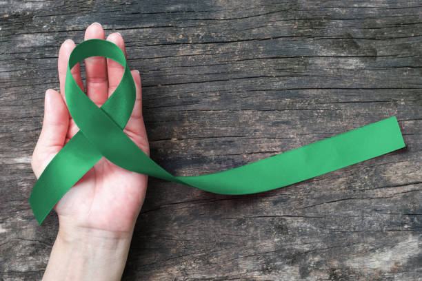 liver cancer awareness wstążka emerald green kolor wstążki na ludzkiej ręce wieku tła, ścieżka przycinania: satynowa tkanina symboliczne logo podnoszenie wsparcia pomóc ludziom życia z chorobą nowotworową - kidney cancer zdjęcia i obrazy z banku zdjęć