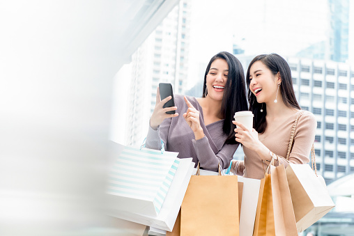 Beautiful young Asian woman friends searching for infomation online via smartphone while shopping in the city