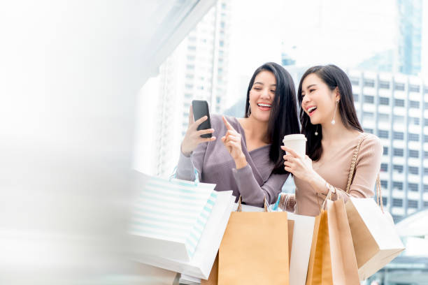Beautiful Asian woman friends using smartphone while shopping in the city Beautiful young Asian woman friends searching for infomation online via smartphone while shopping in the city shopping bag photos stock pictures, royalty-free photos & images