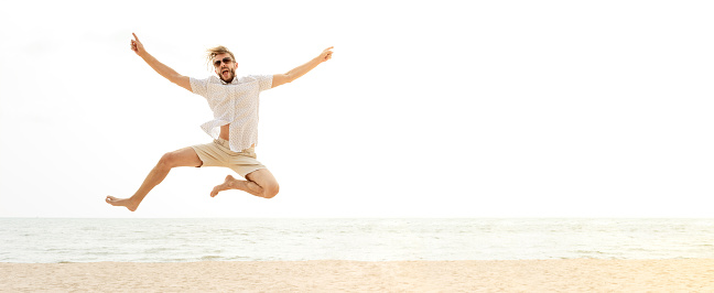 Young energetic happy tourist man jumping at the beach on summer holidays, fun and freedom concepts, panoramic banner with copy space
