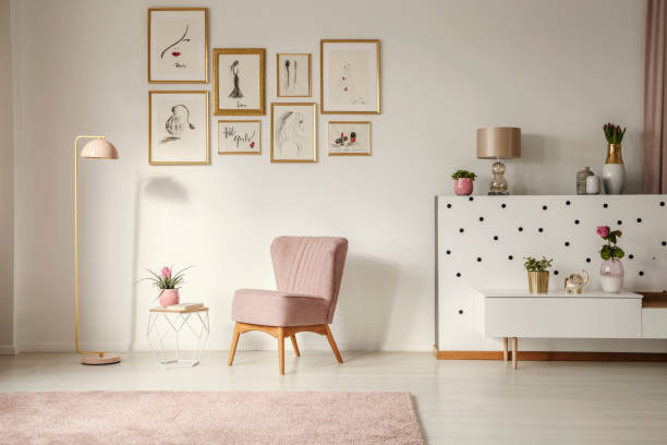 Old-fashioned armchair, pastel pink floor lamp and stylish, golden decorations in a retro living room interior with white walls Old-fashioned armchair, pastel pink floor lamp and stylish, golden decorations in a retro living room interior with white walls femininity photos stock pictures, royalty-free photos & images