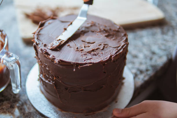 Girl icing a cake A close-up photograph of a girl decorating a cake with chocolate ganache in a domestic kitchen dessert topping photos stock pictures, royalty-free photos & images