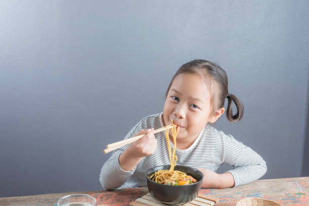 Happy Asian child eating delicious noodle stock photo