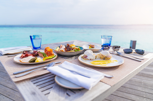 Luxury breakfast food on wooden table, with beautiful tropical Maldives island background, morning time holiday vacation concept.