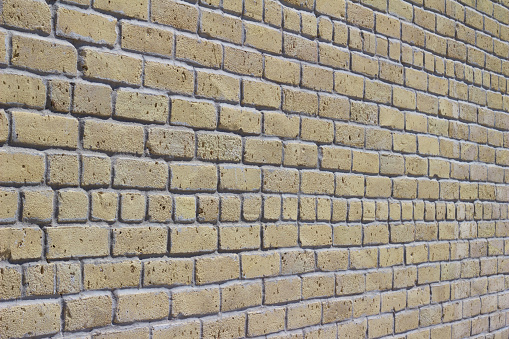 Close up angle view of a rustic antique light beige to white brick wall building background with old weathered bricks in a common bond pattern.