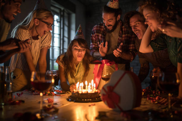 mujer joven soplando velas en una fiesta de cumpleaños en la oficina. - birthday party adult women fotografías e imágenes de stock