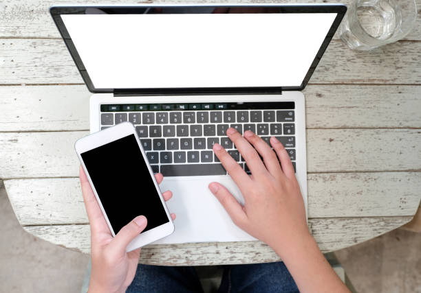 istock Man hands typing laptop computer and smart phone with blank screen for mock up template background, business technology and lifestyle, top view 1001327526