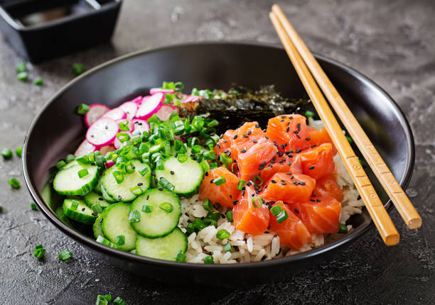Hawaiian salmon fish poke bowl with rice, radish,cucumber, tomato, sesame seeds and seaweeds. Buddha bowl. Diet food stock photo