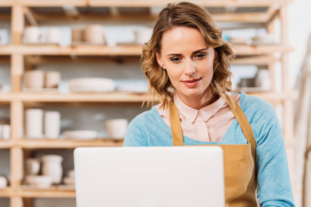 istock beautiful woman in apron using laptop in pottery workshop 1001335518