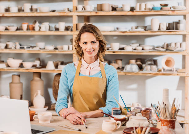 istock happy beautiful potter with ceramics and laptop in workshop 1001341938