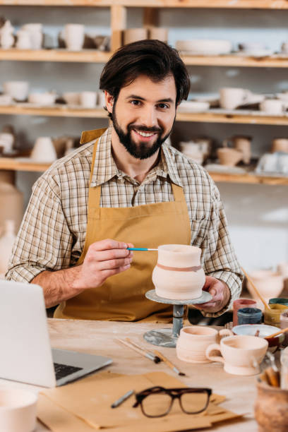 istock happy male potter painting ceramic dishware in workshop with laptop on table 1001342306