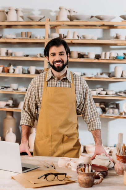 istock smiling male potter in apron standing in workshop with laptop 1001346770