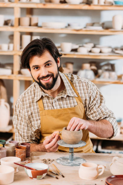 istock smiling potter in apron looking at camera and decorating ceramics in workshop 1001349204
