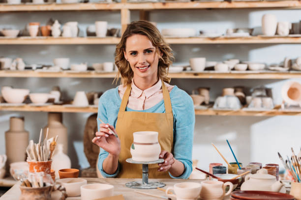 istock smiling woman in apron painting ceramic dishware in pottery workshop 1001349894