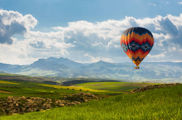 colorido globo aerostático volando sobre el campo verde - heat mid air flying float fotografías e imágenes de stock