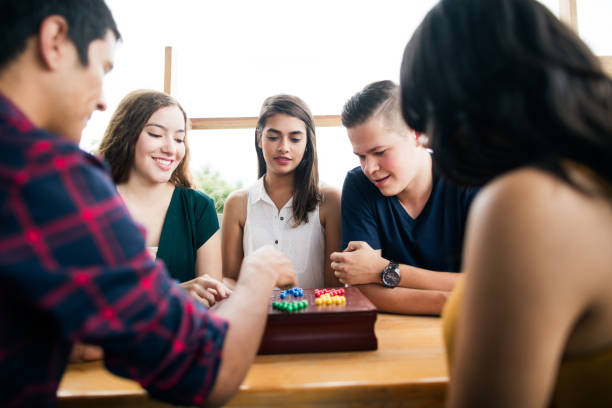 A small group of friends sitting at a table, playing with a board game and enjoying time together.