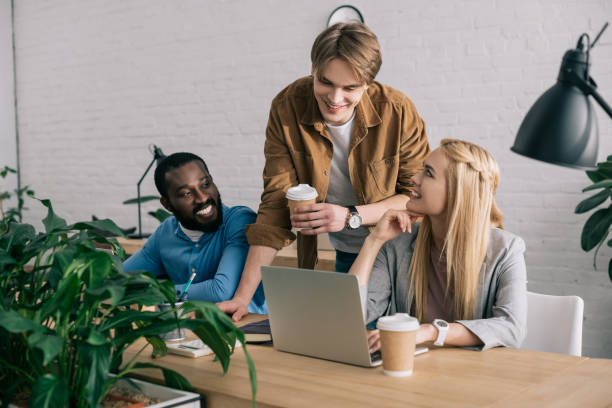 istock smiling multicultural business colleagues with coffee cups talking and watching on laptop 1001354226