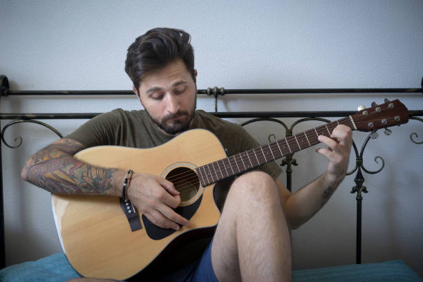 istock Young Man Learn Play Acoustic Guitar in his Bed 1001367626