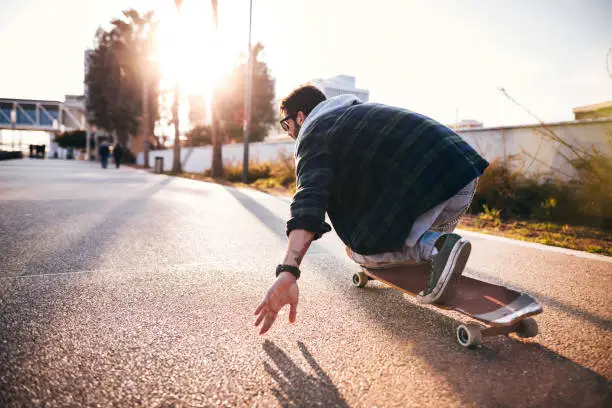 Fashionable professional skateboarder skateboarding with longboard in city park