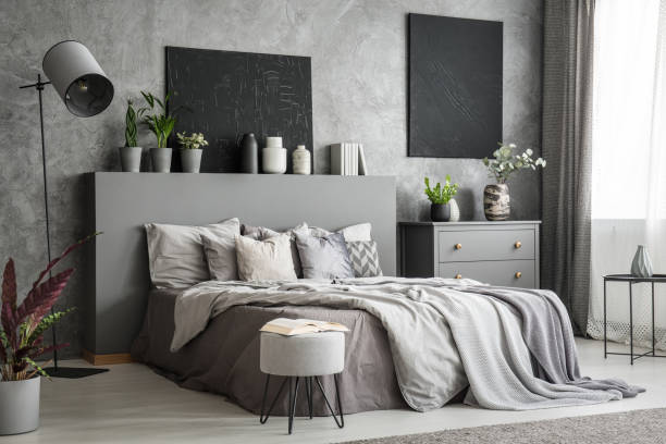 istock Stylish bedroom interior in grey with a big bed with bedsheets, pillows and blankets. A drawer cabinet and a standing lamp against a wall with black paintings. Real photo 1001382954