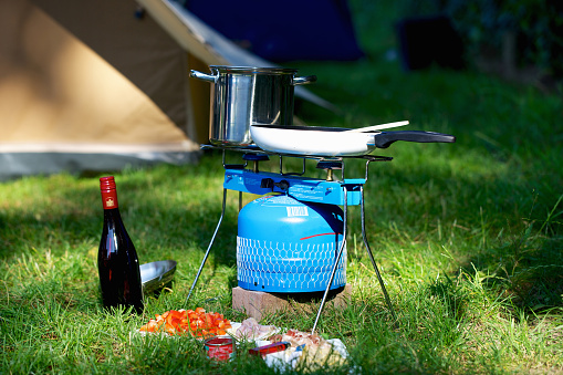 Preparing food outdoors on gas stove in front of tent