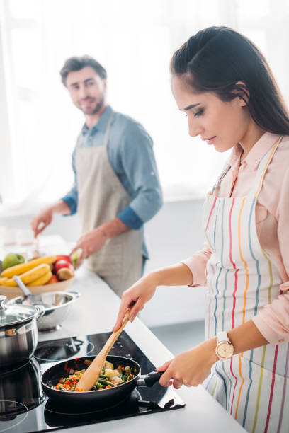 istock girlfriend frying vegetables on frying pan in kitchen 1001386156