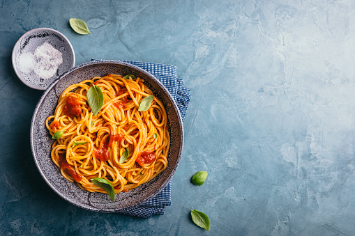 Tasty appetizing pasta served with tomato sauce, fresh tomatoes, basil and cheese in bowl on blue table. View from above