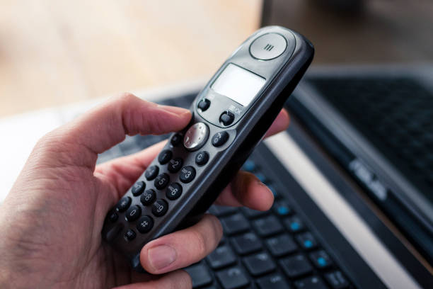 Hand Holding a Black Cordless Telephone with Laptop at Background Hand holding a black cordless telephone with a laptop at the background cordless phone stock pictures, royalty-free photos & images